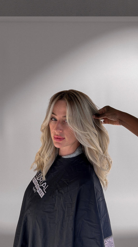 On voit une femme blonde, avec une couleur lumineuse, éclatante et brillante. Elle vient de se faire couper les cheveux et elle a la cape de chez le coiffeur. 